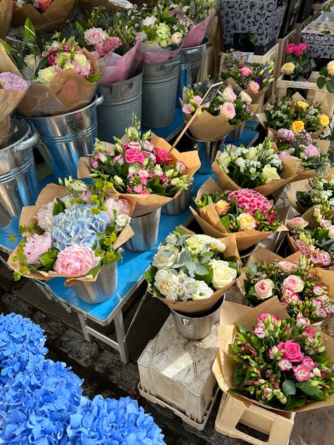 An array of fresh floral bouquet arrangements displayed on a table at a flower market, featuring a variety of flowers including pink roses, white hydrangeas, pale pink peonies, and light blue hydrange